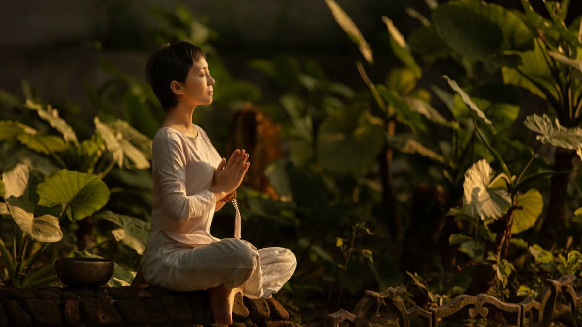Serene scene of a woman meditating in a lush garden setting at daylight.